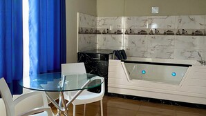 Una cocina moderna con una mesa de comedor de vidrio, sillas blancas, encimera negra y salpicadero de mármol.