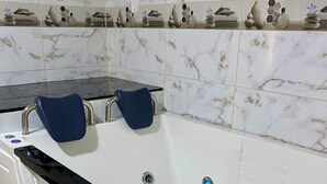Un baño moderno con una bañera blanca, grifos negros y paredes con diseño de mármol.