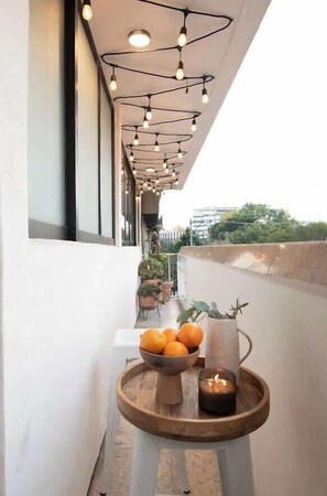 Ein Balkon mit Lichterketten, einem kleinen Tisch mit Orangen und einer Kerze sowie Kübelpflanzen.