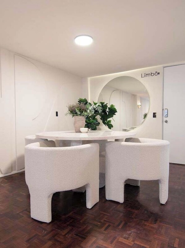 A white dining table with two chairs, a potted plant, and a mirror on the wall.