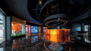 Un vestíbulo moderno con un bar central, una gran pantalla digital y un suelo reflectante.