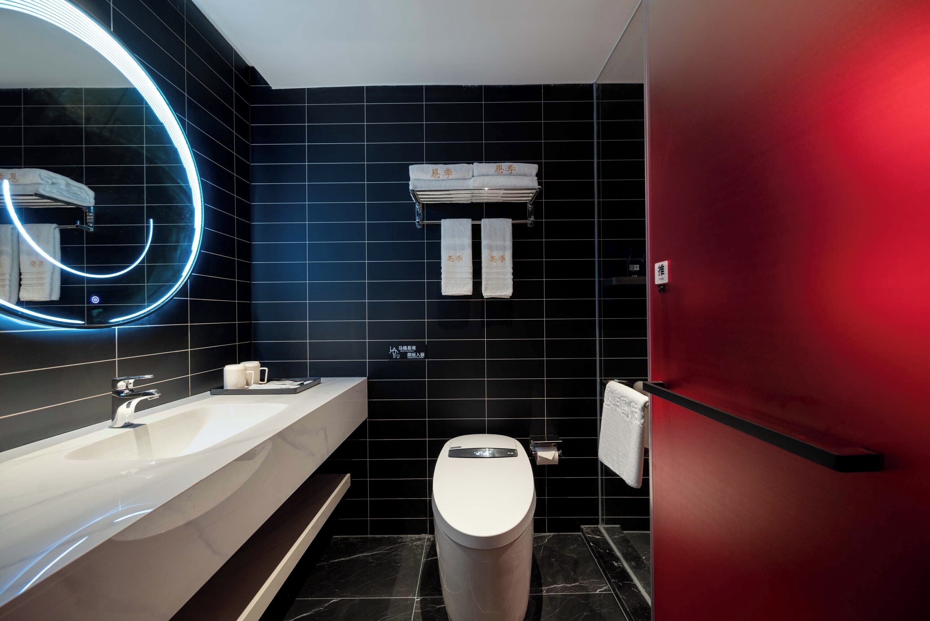 A modern bathroom with a white sink, a toilet, and a red wall. There is a towel rack with two towels and a sign with Chinese characters.