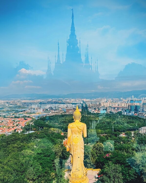 Una gran estatua dorada de Buda domina un paisaje urbano con un templo destacado al fondo.