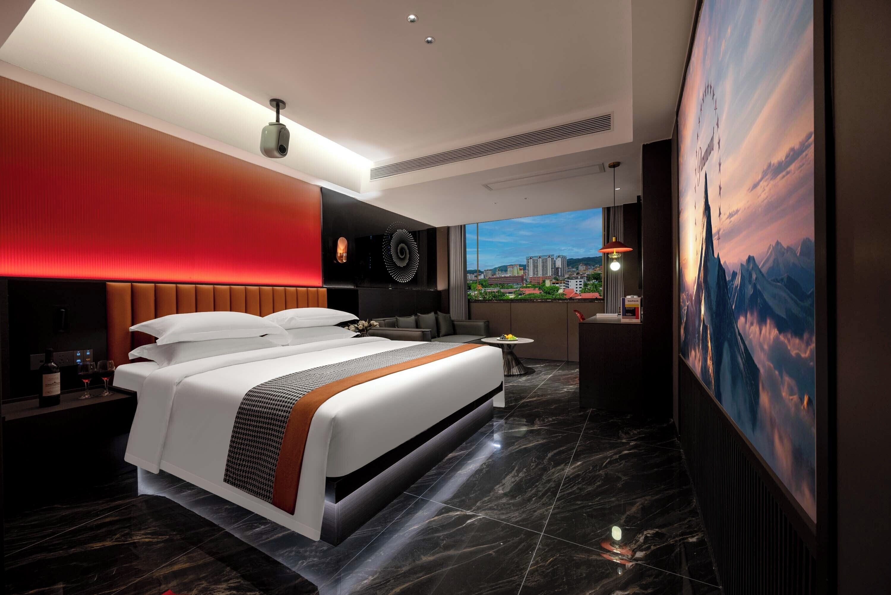 A modern hotel room with a large bed, a city view, and a large painting of a mountain landscape.