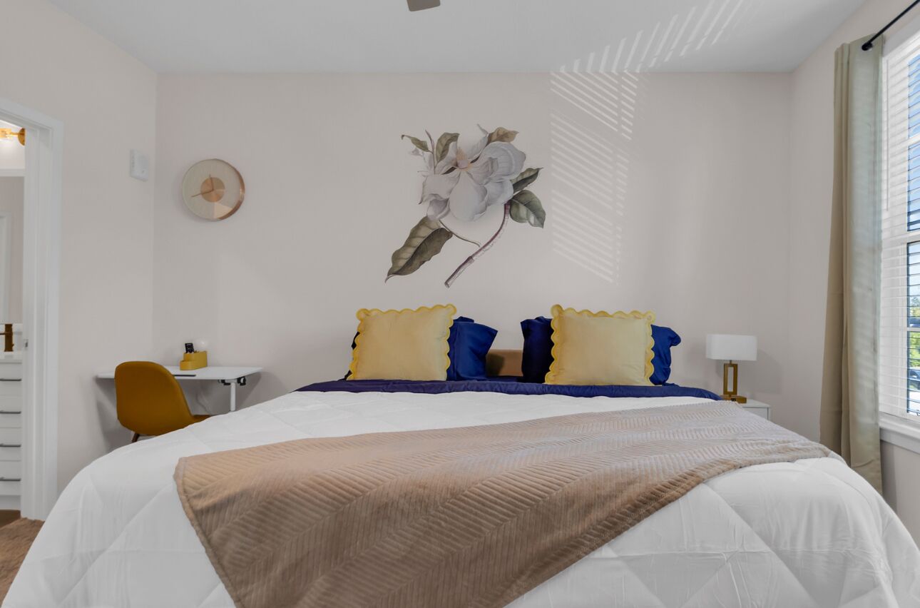 A bedroom with a bed, a desk, a chair, and a wall-mounted clock.