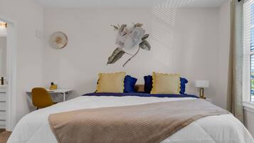 A bedroom with a bed, a desk, a chair, and a wall-mounted clock.