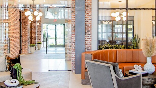 Een ruime lobby met een hoge plafond, openliggende bakstenen muren en moderne verlichtingsarmaturen.