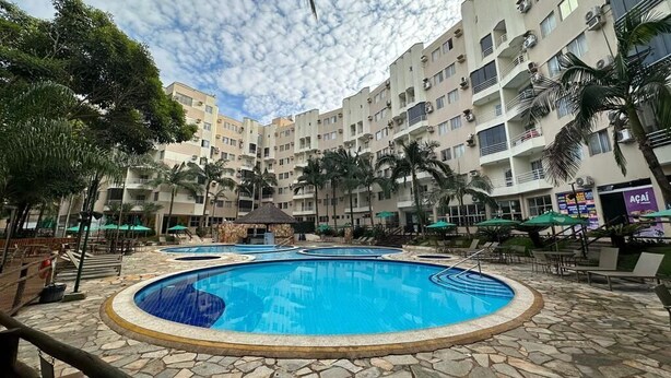 Una piscina circondata da piastrelle di pietra, con palme e un edificio a più piani sullo sfondo.