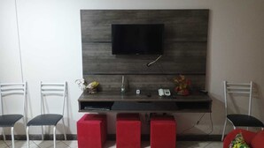 Una camera moderna con una TV a schermo piatto montata su una parete in legno scuro, una scrivania con un telefono e due sgabelli imbottiti rossi.