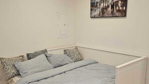 A bedroom with a bed, pillows, a radiator, and a painting on the wall.