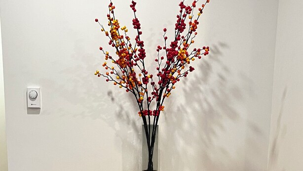 A wooden table with two benches, a vase with branches and berries, and a plain wall.