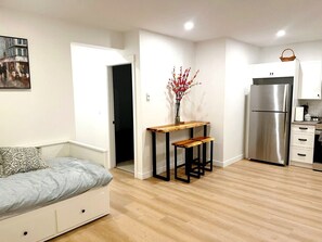 A compact living space with a sofa, a wooden table with benches, a refrigerator, and a kitchen area. - Modern Suite in Willoughby Langley Private Entry Full Kitchen Fast WiFi (Langley Township)