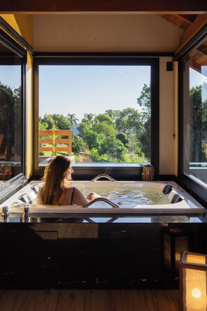 Une femme se détend dans une baignoire, avec vue sur des arbres et une chaise en bois.