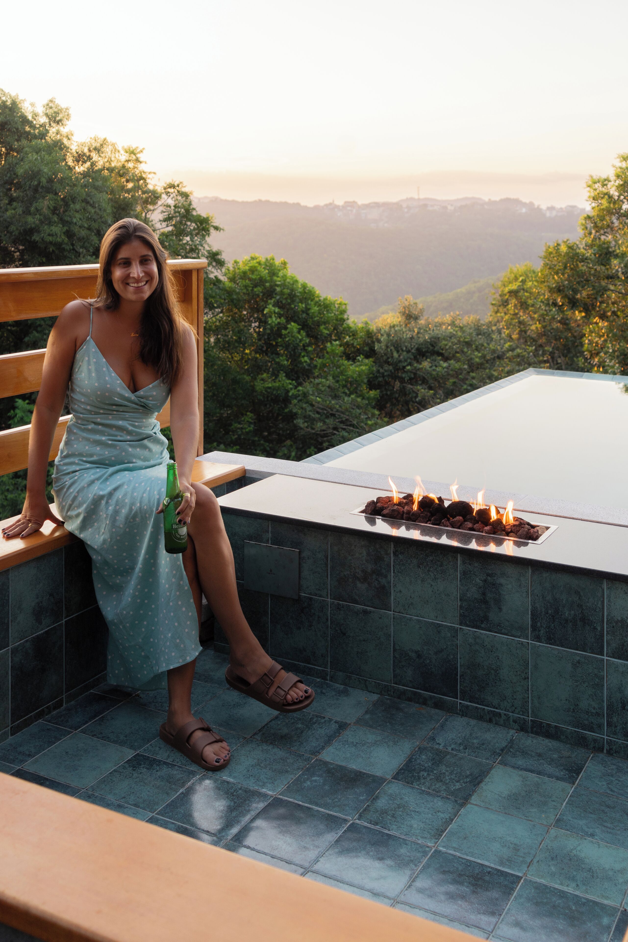A person seated on a wooden bench overlooking a pool with a fire feature.