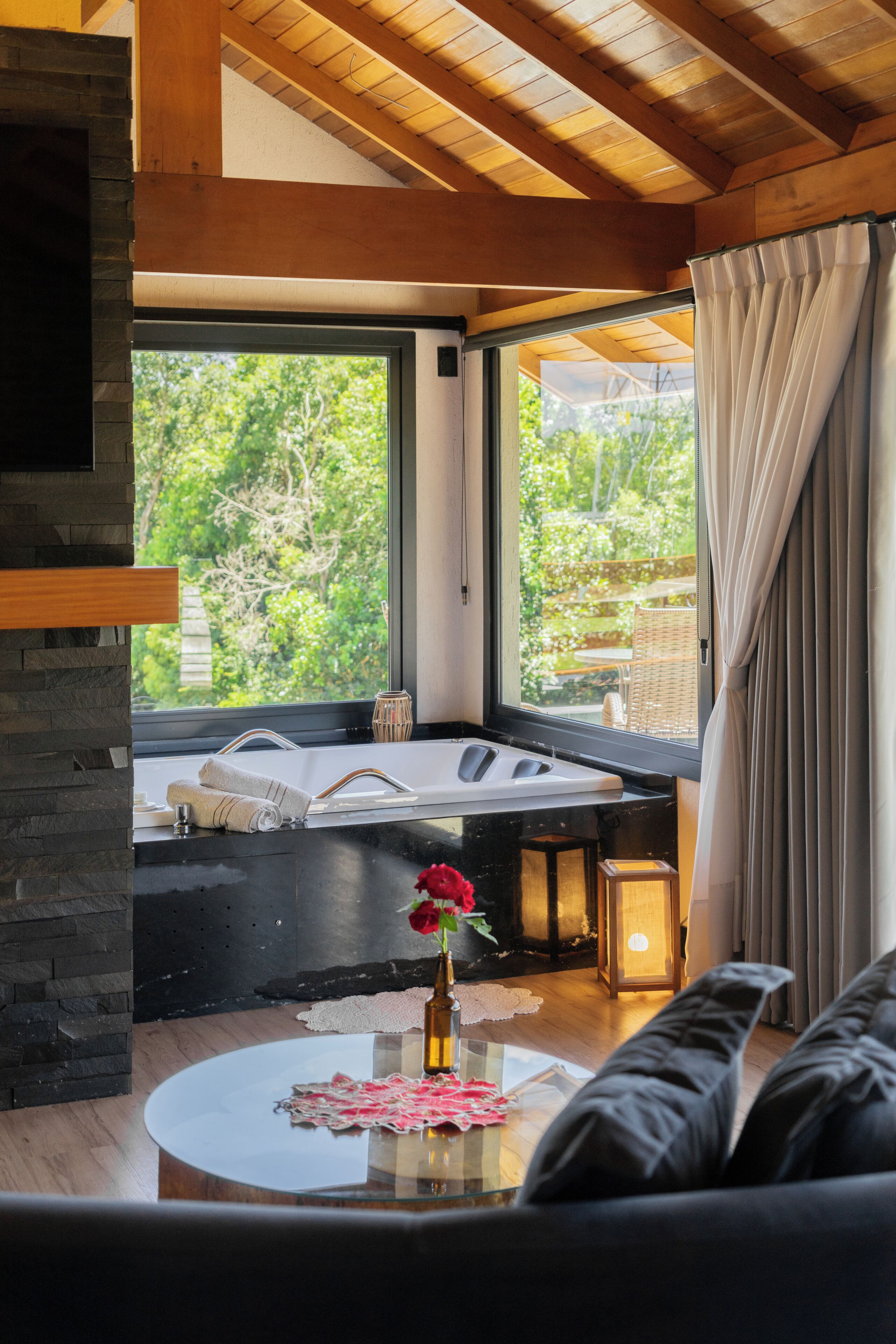 A modern bathroom with a bathtub, a window with a view of greenery, and a glass table with a vase.