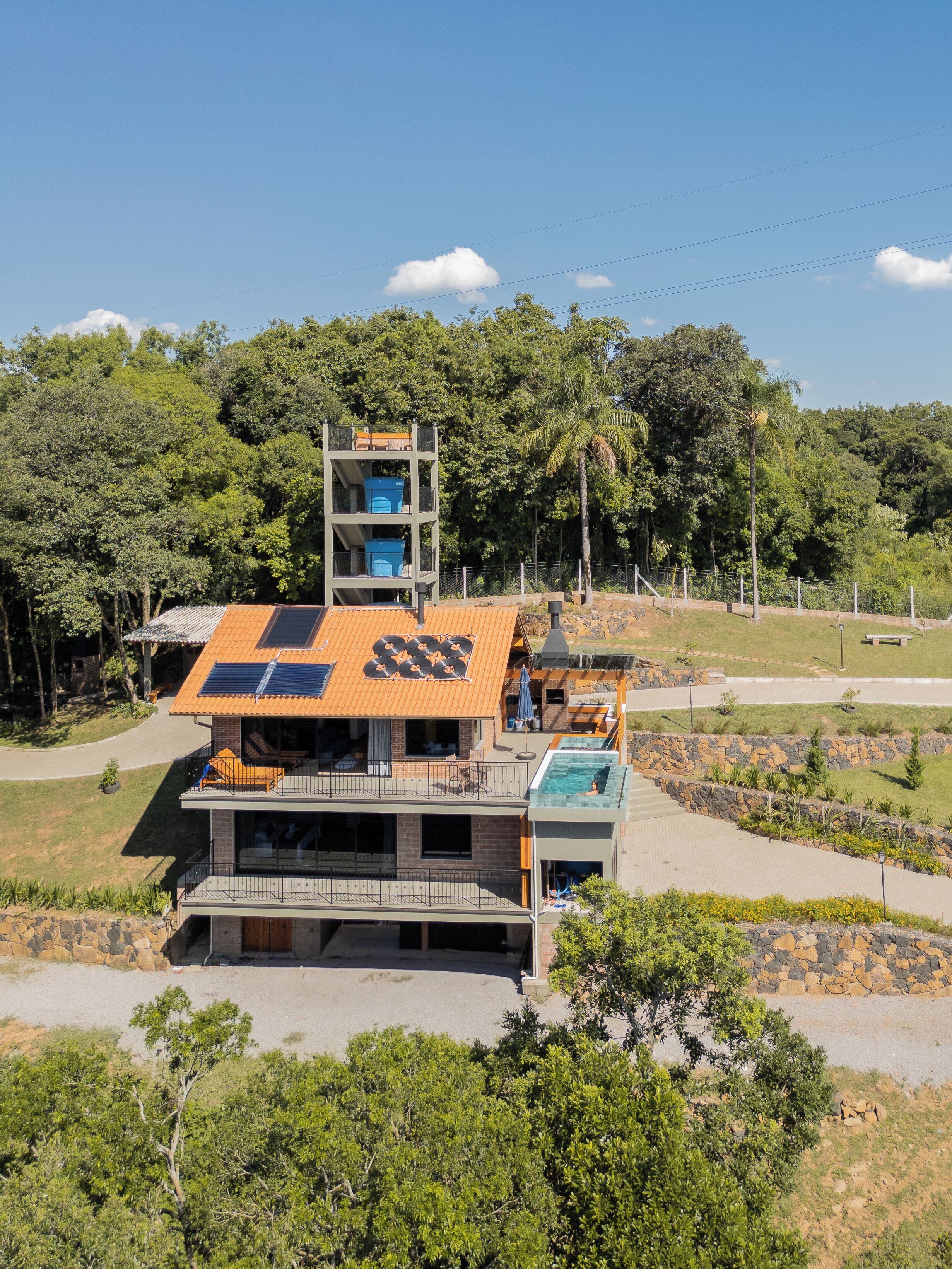 Una casa moderna de varios pisos con piscina en la azotea, un espacio exterior cubierto y vistas a la vegetación circundante.