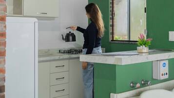 Een keuken met een groene wand, witte kasten, een witte koelkast en een raam met een witte luxaflex.
