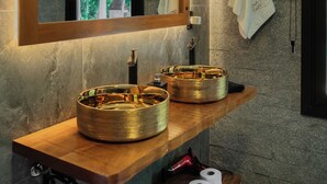 Een badkamer met een houten wastafelmeubel, twee gouden wastafels, een spiegel en een handdoek aan de muur.