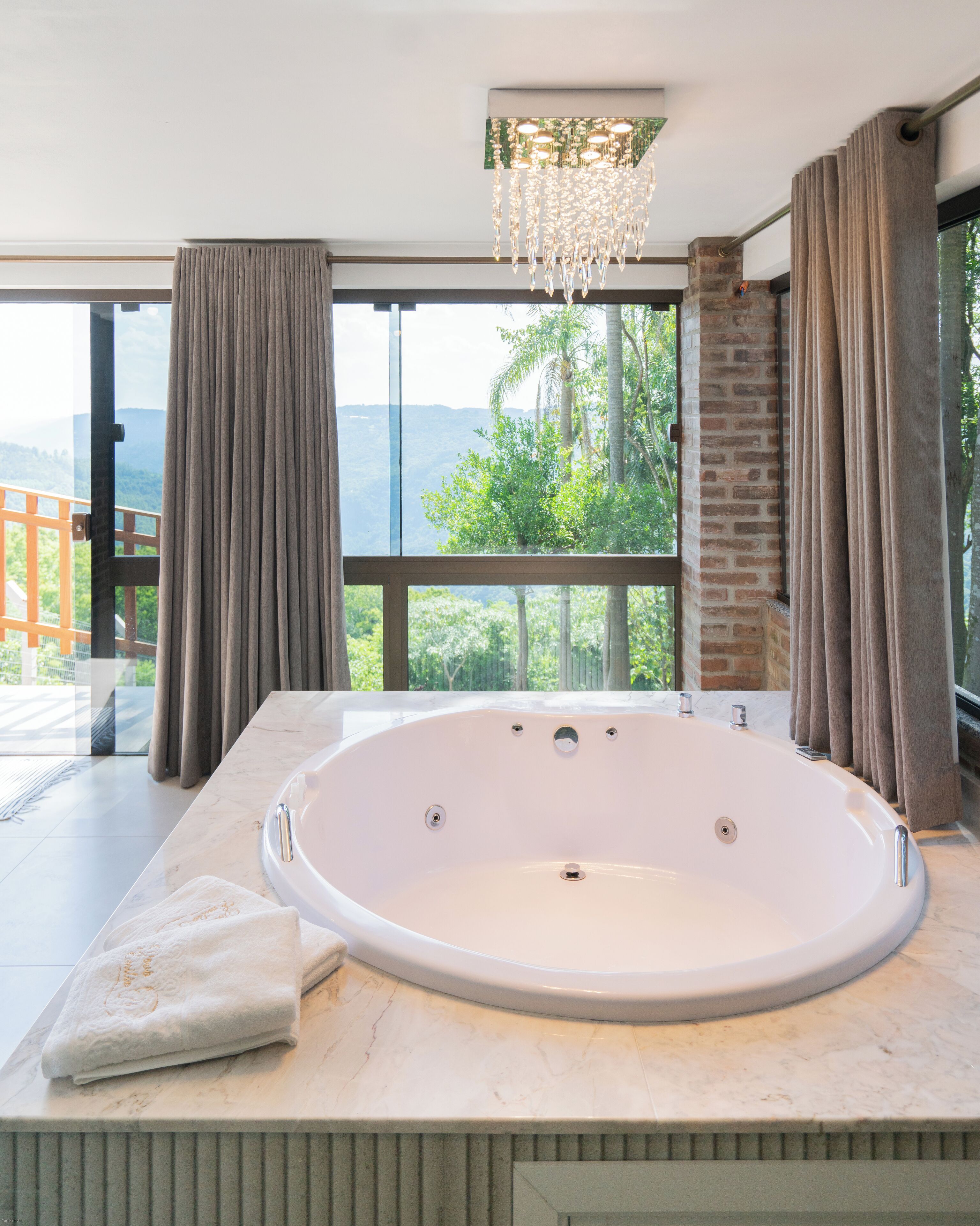 Une salle de bain moderne avec une grande baignoire, un lustre et une vue sur l’extérieur.