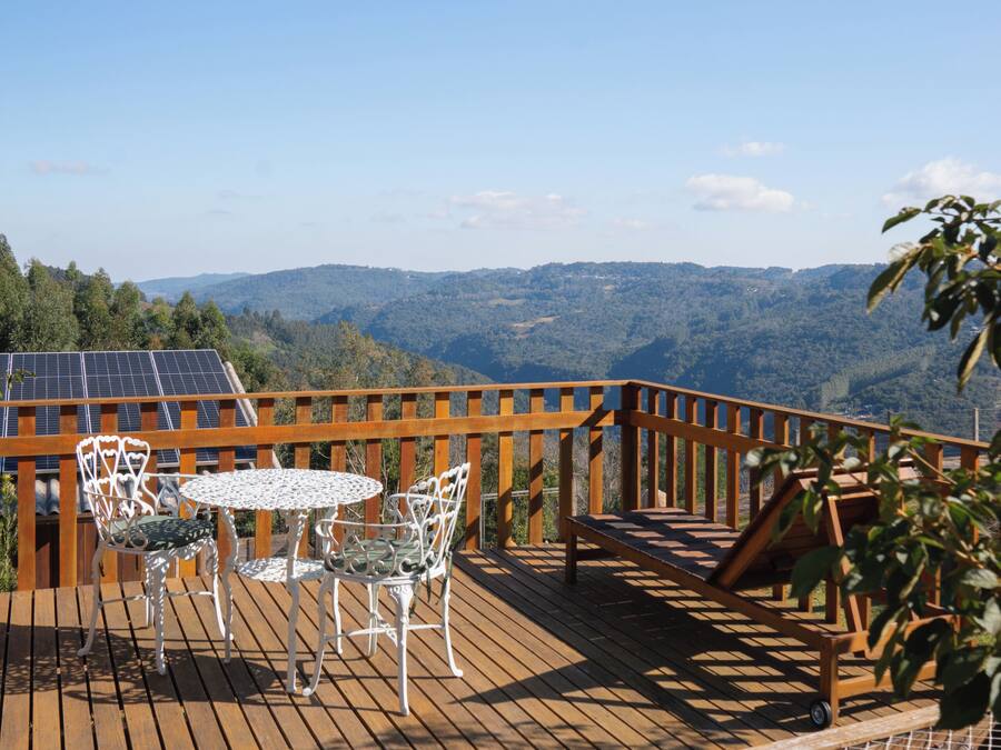 Una terraza de madera con una mesa y sillas, un pequeño rincón de descanso y vistas a las montañas.