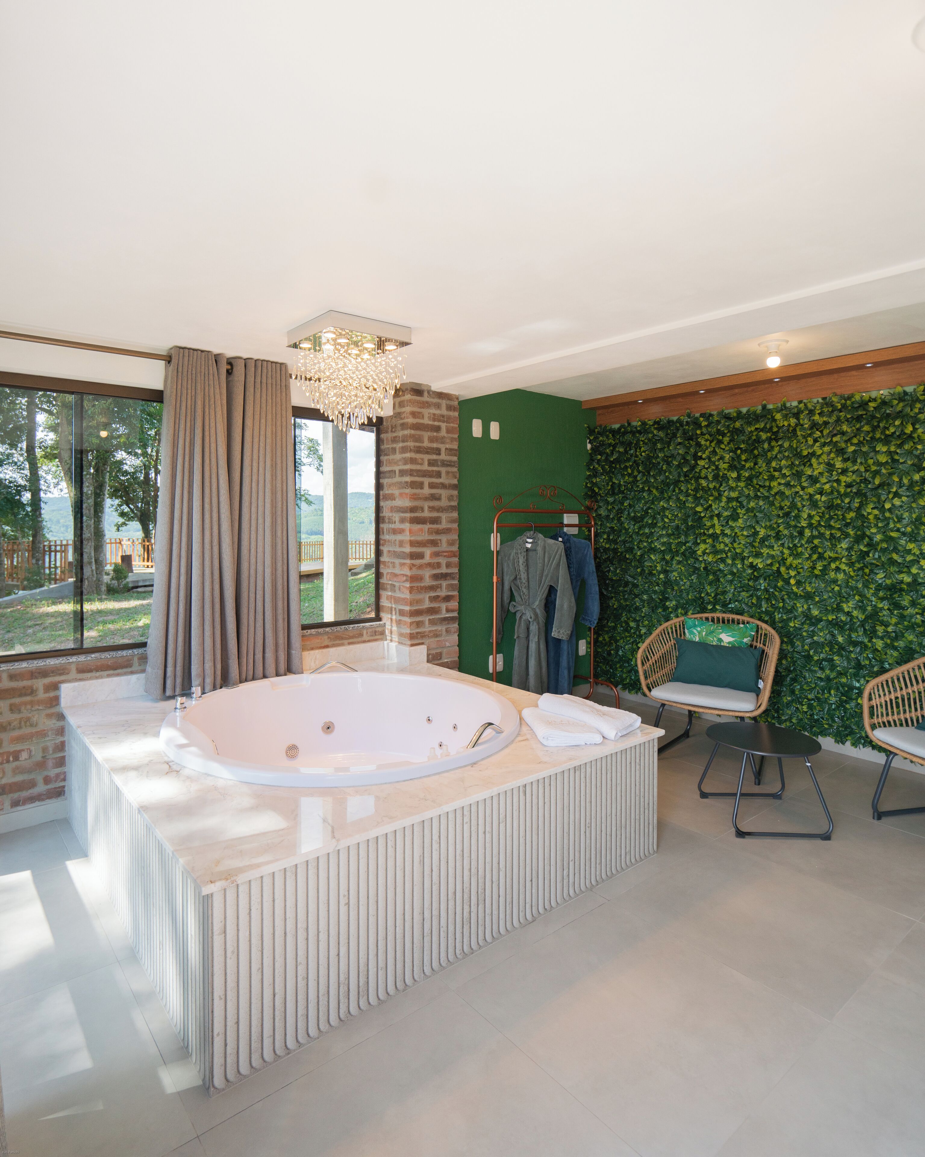 Un baño moderno con una bañera grande, una pared verde, sillas de mimbre y vistas al exterior.