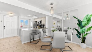 Une cuisine moderne dotée d’un îlot central, d’un coin repas avec une table et des chaises en verre, et d’une grande plante en pot.