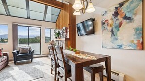 A dining area with a wooden table and chairs, a TV mounted on the wall, and a large abstract painting. - Beaver Run 28220: Ski-In/Out Peak 9 Condo, Fireplace, Pools & Hot Tubs. (Breckenridge)