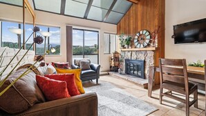 A spacious living room with a fireplace, a large window, and a television mounted on the wall. - Beaver Run 28220: Ski-In/Out Peak 9 Condo, Fireplace, Pools & Hot Tubs. (Breckenridge)