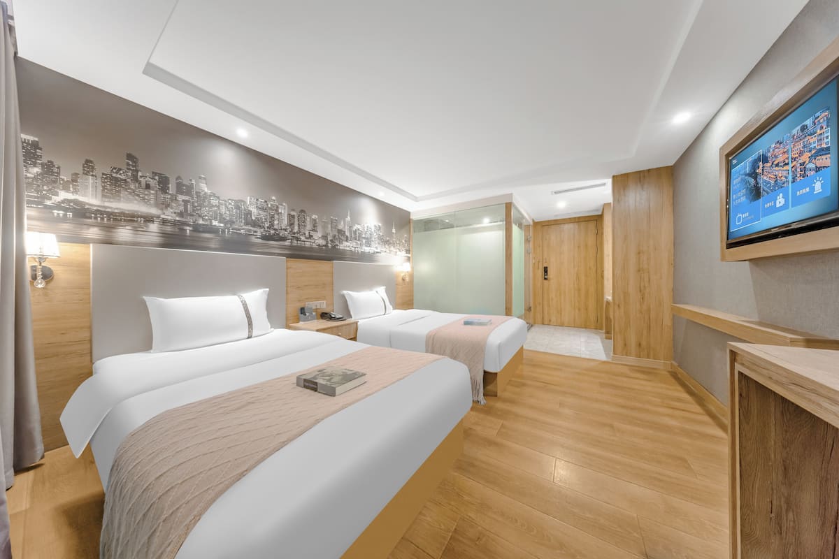 A hotel room with two beds, a cityscape mural, a television, and wooden flooring.
