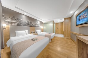 A hotel room with two beds, a cityscape mural, a television, and wooden flooring.