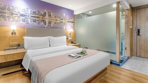 Hotelkamer met een groot bed, een stadsgezicht muurschildering, een houten hoofdbord, een nachtkastje met een lamp en een douchecabine van glas.