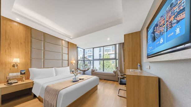 Een moderne hotelkamer met een groot bed, een houten hoofdbord, een bureau en een televisie waarop een stadsgezicht te zien is.