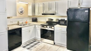 A modern kitchen with white cabinets, a black refrigerator, a stove, an oven, and a microwave.