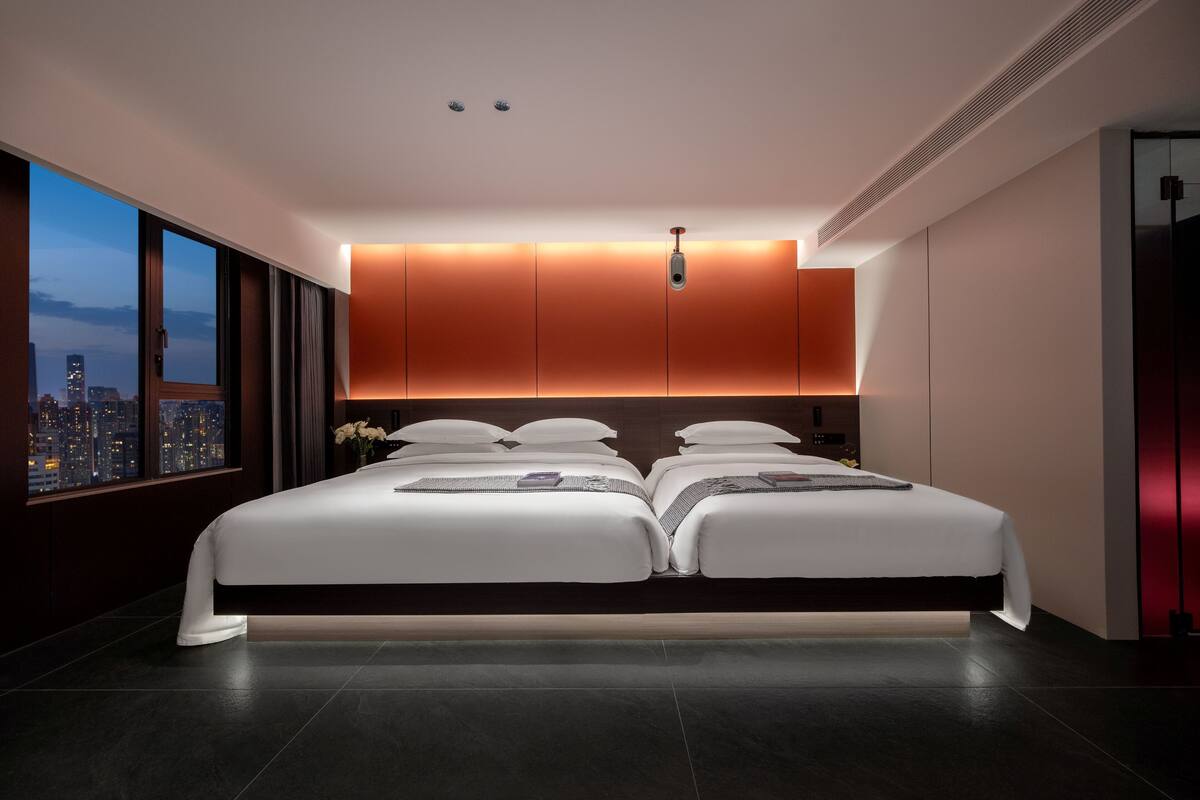 A modern hotel room with a large bed, city view, and ambient lighting.