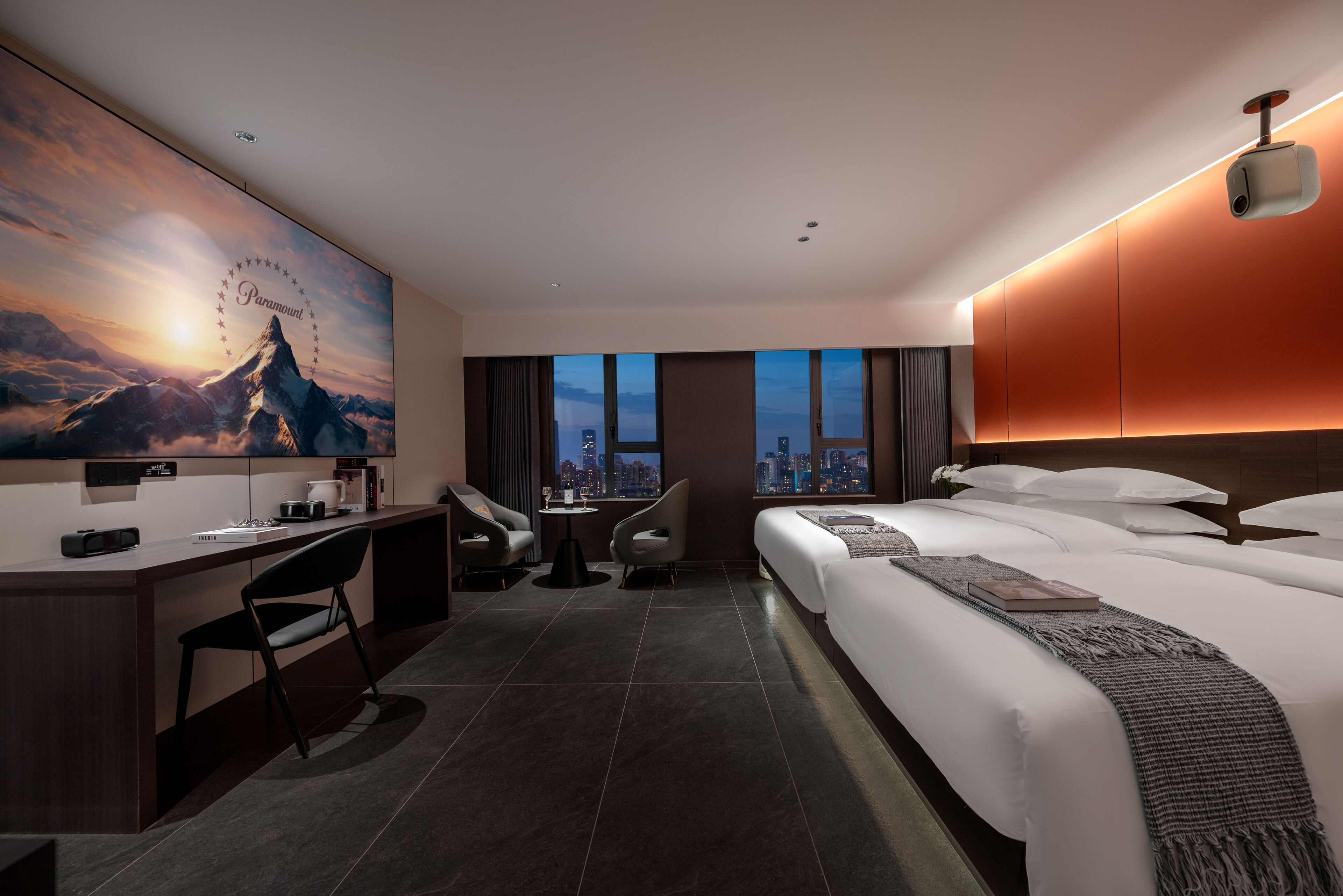 Habitación de hotel moderna con una cama grande, un escritorio, una silla, una mesita y vistas a la ciudad a través de las ventanas.
