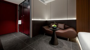 Ein modernes Hotelzimmer mit roter Tür, einem braunen Sofa, einem kleinen Tisch mit einer Vase und einem weißen Bett.