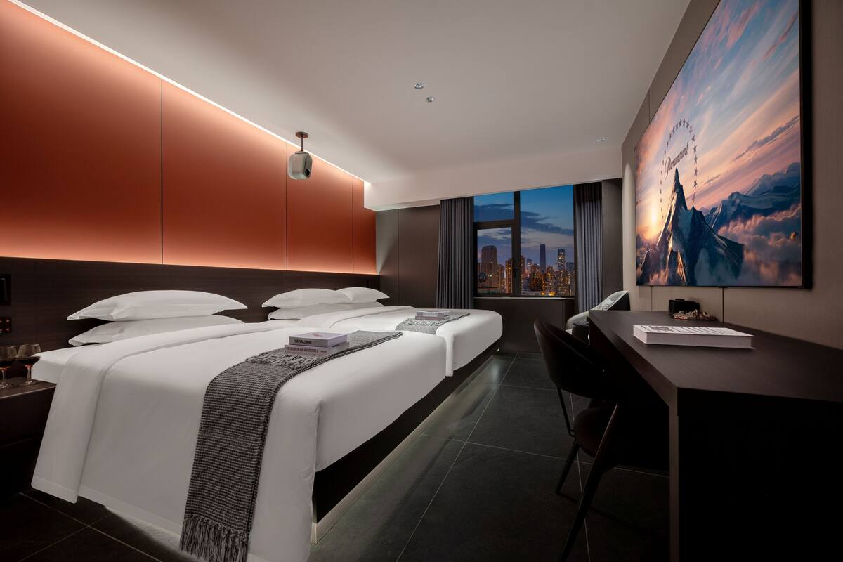 A modern hotel room with a large bed, a desk, and a cityscape view.