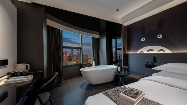 Ein modernes Hotelzimmer mit einem großen Bett, einer Badewanne, einem Schreibtisch mit Stuhl und Blick auf die Stadt.