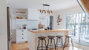 A modern kitchen with a central island, bar stools, and a large window with a view of trees. - Cedar Sauna, Cedar Hot Tub, Lakeside Fire Pit, Private Beach | La Dolce Muskoka (Bracebridge)
