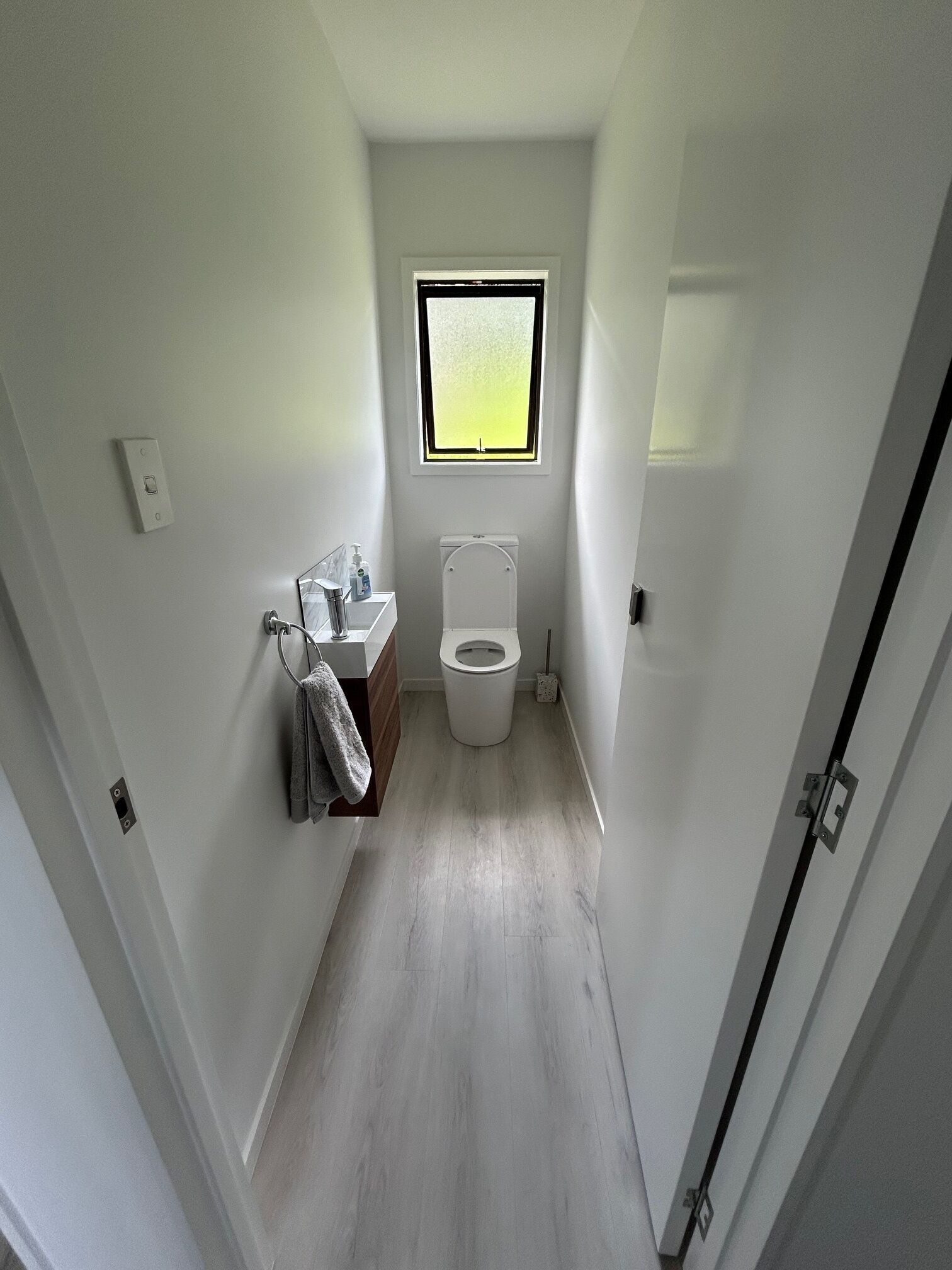 A narrow bathroom with a toilet, a sink, and a window.