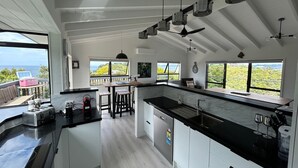 A modern kitchen with a large island, black countertops, and a view of the ocean. - Te Puawaitanga Beach House - The Blossoming of Something New. (Tutukaka)