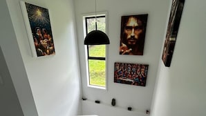 A staircase with a modern design, white walls, and artwork on the walls. - Te Puawaitanga Beach House - The Blossoming of Something New. (Tutukaka)