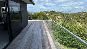 A wooden deck with a glass balustrade overlooking a lush landscape. - Te Puawaitanga Beach House - The Blossoming of Something New. (Tutukaka)