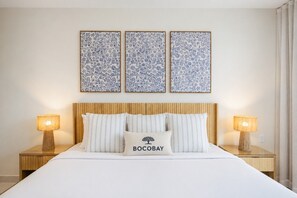 A neatly made bed with a white comforter and striped pillows, flanked by two bedside tables with lamps, and three framed floral artworks above. - Luxury 4BR Villa | Private Pool | Steps to Beach - Costa Catalina 2 by Bocobay (Noord)