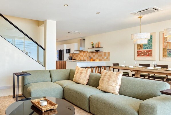 A modern living room with a sectional sofa, a coffee table, and a dining area with a long table and chairs.
