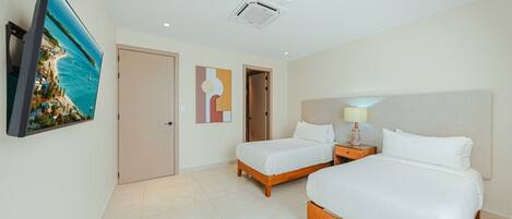 Quarto de hotel com duas camas, uma televisão, uma ventilação no teto e uma porta.