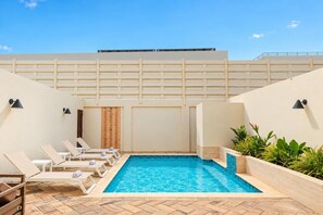 A swimming pool with lounge chairs, a tiled floor, and a wall with a balcony.
