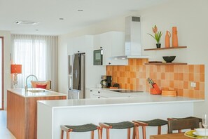A modern kitchen with a central island, stainless steel appliances, and a checkered backsplash. - Luxury 4BR Villa | Private Pool | Steps to Beach - Costa Catalina 2 by Bocobay (Noord)