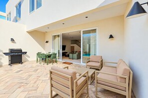 Um pátio externo com churrasqueira, área de estar e vista para a piscina.