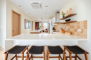 A modern kitchen with a central island, wooden chairs, and a tiled backsplash.